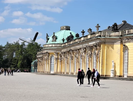 Schloss Sanssouci, Potsdam, blauer Himmel, Sonnenschein, Menschen laufen vor dem Schloss entlang